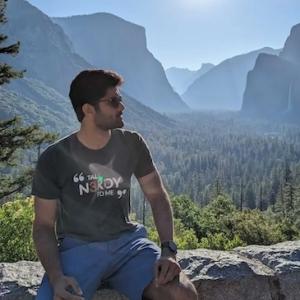 Manoj seated on a wall with a vista of the mountains behind him.