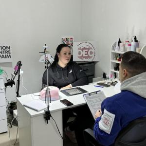 Woman sits and desk across from man. 