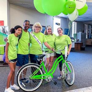 Mary Lou Schlueter and family pose in green t-shirts behind a green bike and balloons