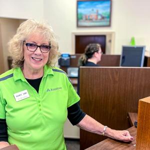 Mary Lou Schlueter in a green shirt at a teller's station