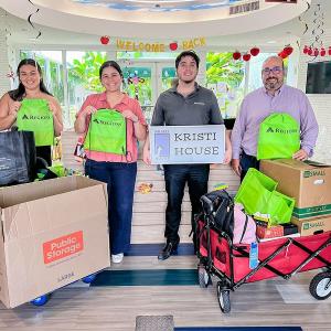 Four people posed with Regions bags, and a sign for Kristi House. Boxes of supplies in front.