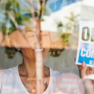 Woman in a glass window putting up an Open, Come in sign.