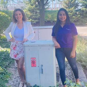 Two people posed next to an outdoor electrical box.