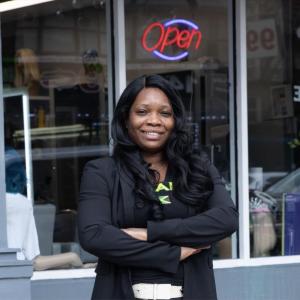 Mitzie outside of a store with a lit "Open" sign.