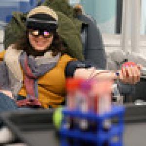A person reclined and donating blood. They are wearing a VR headset and smiling.