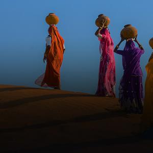 Women carrying pots of water across a desert.