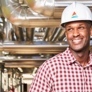 A person in a hardhat with southern company logo, underneath industrial piping. They are smiling and wearing a white and red checked button up shirt.