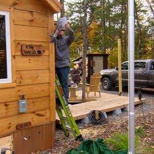 a person installing equipment on the side of a home in a wooded area. A grey truck behind them.