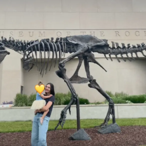 Natalie and her daughter in front of a fossil of a dinosaur.