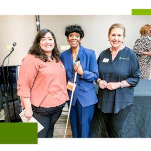 A woman in a blue suit holding a white mobility cane surrounded by 2 bank representatives