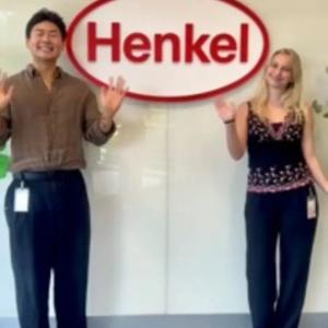 two interns waving in front of Henkel sign