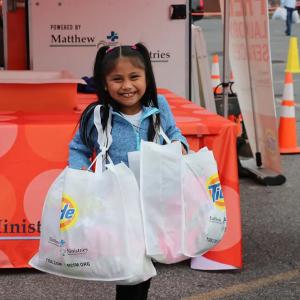A child holding two bags with Tide logos on them, an orange table behind her.