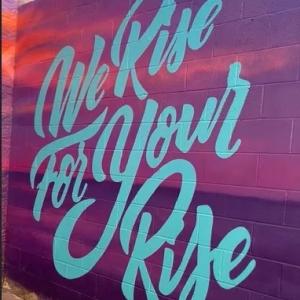 sign reading, "We Rise For Your Rise"