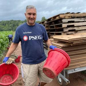 Man wearing a PSEG shirt, outside at a farm holding two large buckets