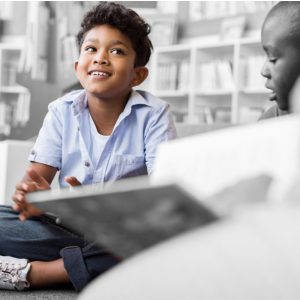 a student in color seated on the floor, everything else is in black and white. Book shelves behind them.