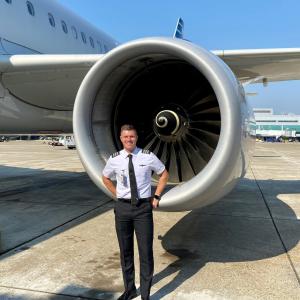 Pilot David Pettet standing in uniform in front of a plane engine