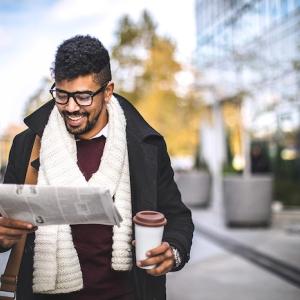Person reading newspaper while holding coffee