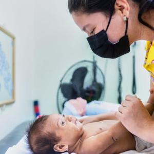 An adult leaning over a baby on a doctor's table.