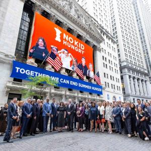 Group of supporters for No Kid Hungry standing outside No Kid Hungry banner on the front of the New York Stock Exchange