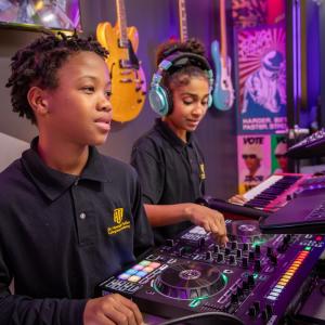 Young people use DJ equipment, a keyboard and headphones in a colorful music production studio.
