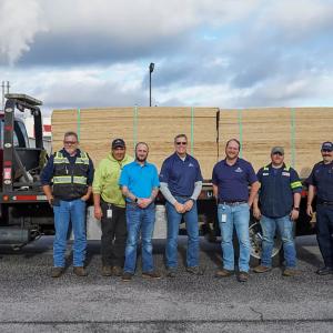 A group of seven people in front of a truck with loads of OSB boards on the trailer.