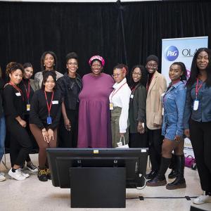 A group of women on a stage with black curtains behind. A floor monitor in front of them