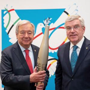 Two people stood next to each other wearing suits, the person on the left is holding the Olympic torch 
