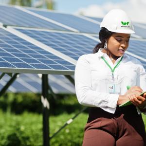 Female Wesco employee shown with a clipboard in front of a solar panel array.