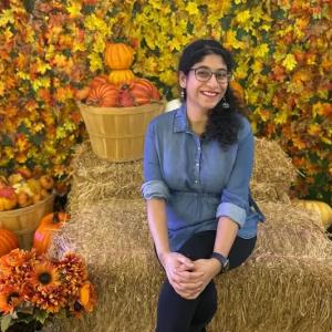 Sanjana seated on a bale of hay with pumpkins around her.