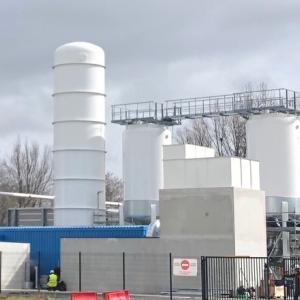 A fenced off industrial area with tanks, tubing, small buildings.