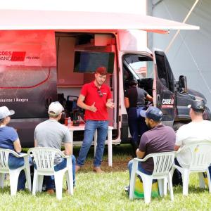 A group of people in white chairs listening to a presenter, an open truck behind them with an awning, CaseIH logos.