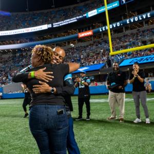 Hip Hop Smoothies of Charlotte representative hugs Lenovo North America CMO Gerald Youngblood on the Carolina Panthers field