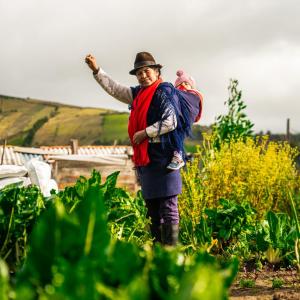 farmer stands in a field her baby strapped to her back