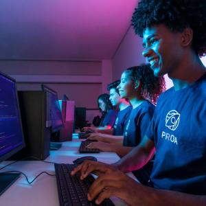 Students at a long table in a dark room, each using a desktop computer.