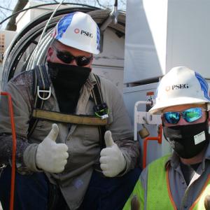 Two PSEG technicians; wearing helmets and masks giving the thumbs up sign.