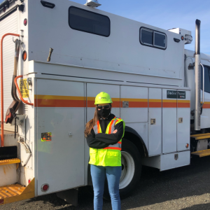 PSEG female employee standing in front of a PSEG service vehicle wearing safety gear, mask and hardhat.