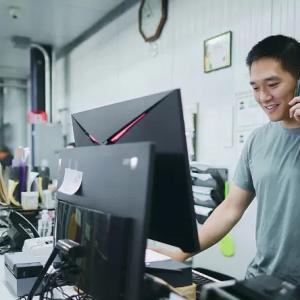A person stood at a table, looking at a monitor while on the phone
