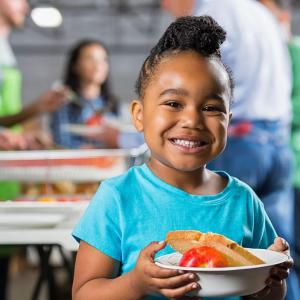 A young child smiling while holding a bowl of food