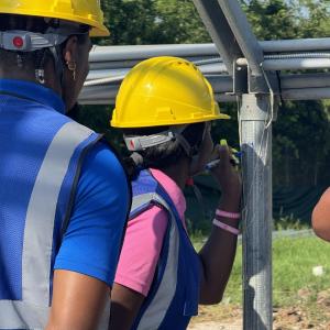 Girl in construction vest and hard hat signs greenhouse post with permanent marker.