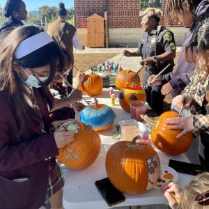 Group of high school students and police officer painting pumpkins