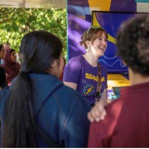 A woman in a MilliporeSigma Spark T-Shirt smiles alongside students. 
