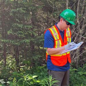 Chris Reeves standing in a forest reviewing papers.