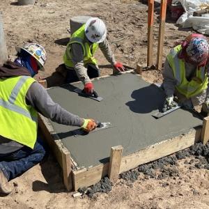 Three construction workers smoothing a square of concrete