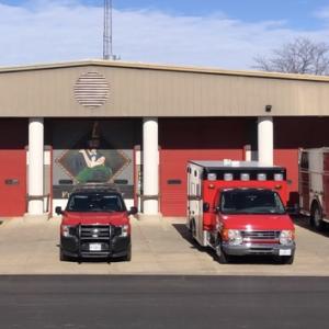 A row of first response and fire vehicles lined up outside a fire station.