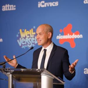 A speaker stood at a stand, talking into a microphone at the “Well Versed” premiere