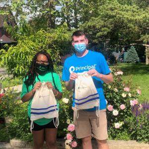 A young man and young woman; wearing face masks are holding a white bag in a garden.