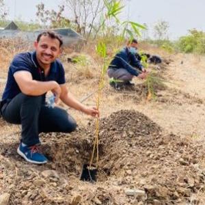employee bends down next to tree sapling
