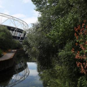 A scenic river view, runners on a pathway along side it. A stadium in the background.
