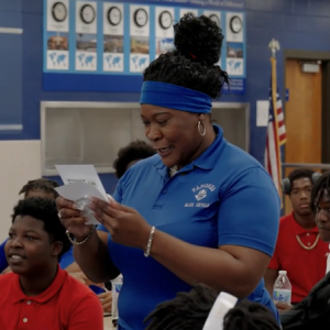 Woman reading a letter to a class of students. 
