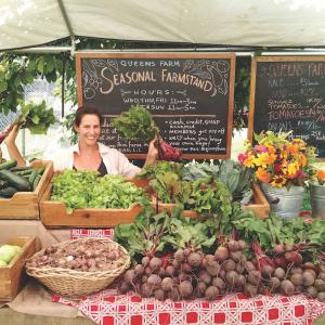 Person sitting at a farm stand covered in vegetables at Queens County Farm Museum